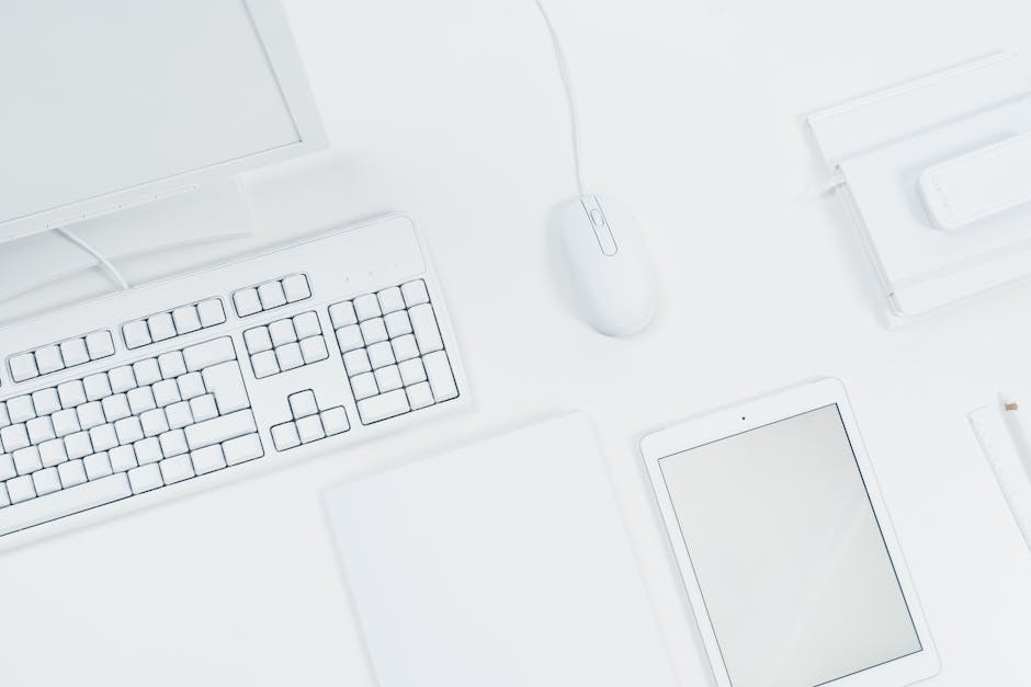 A clean, minimalist workspace featuring a keyboard, mouse, and tablet on a white desk.