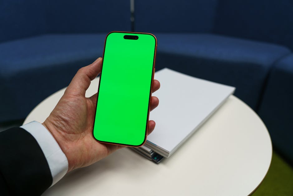 Corporate individual holding a smartphone with a chroma key green screen in an office setting.