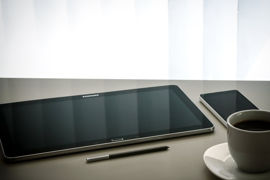 Minimalist office desk setup featuring a tablet, smartphone, pen, and coffee cup on a reflective surface.