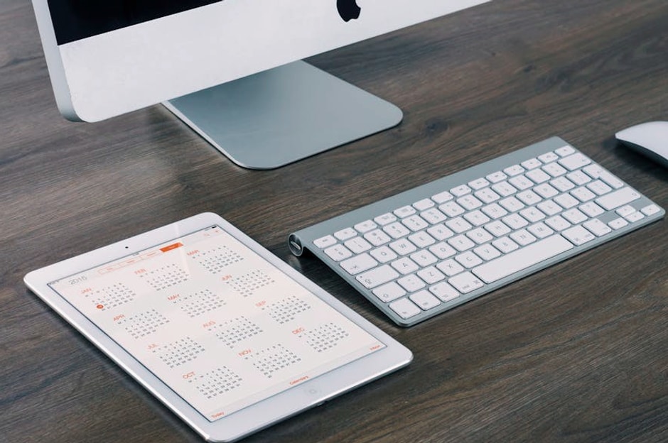 A sleek and modern office desk setup featuring an iMac, iPad with calendar, keyboard, and mouse.