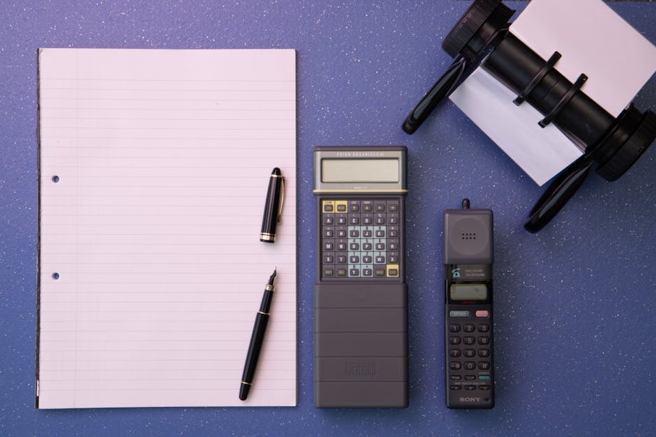 Flat lay of vintage office items including a calculator, mobile phone, and paper on a blue background.