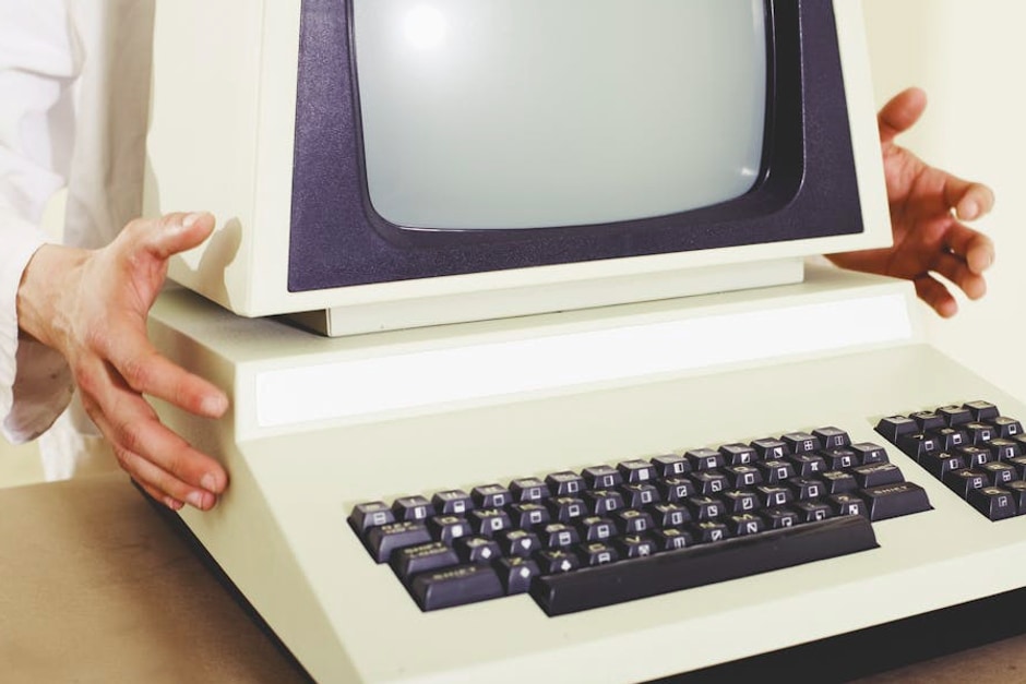 A vintage computer with a classic CRT monitor and keyboard, being held by hands.