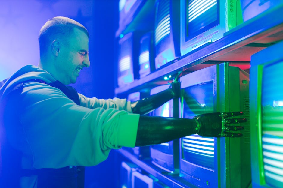 Smiling man with prosthetic arm adjusts retro TVs in a neon-lit setting.