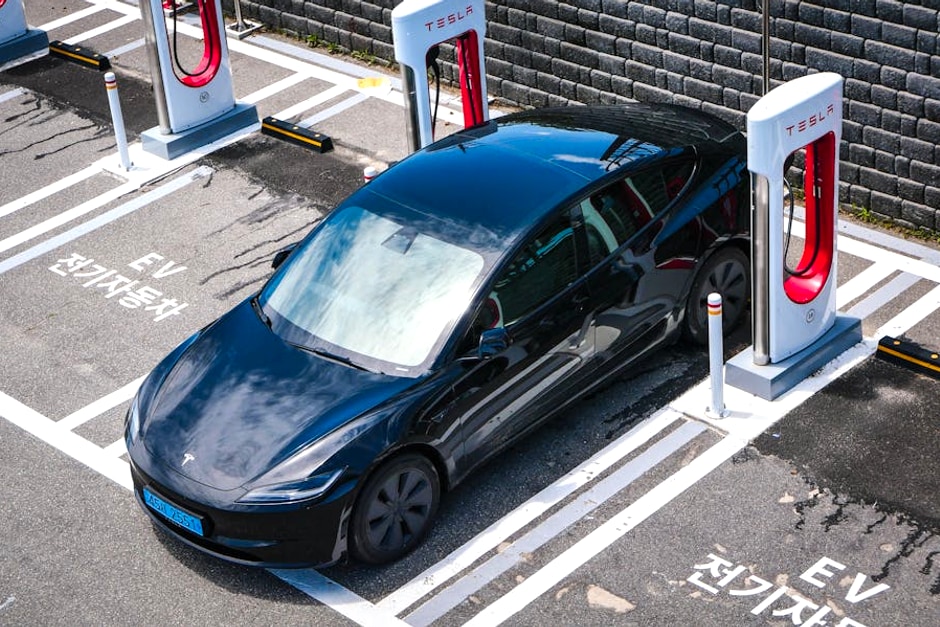 A black Tesla parked at a charging station in an urban setting.