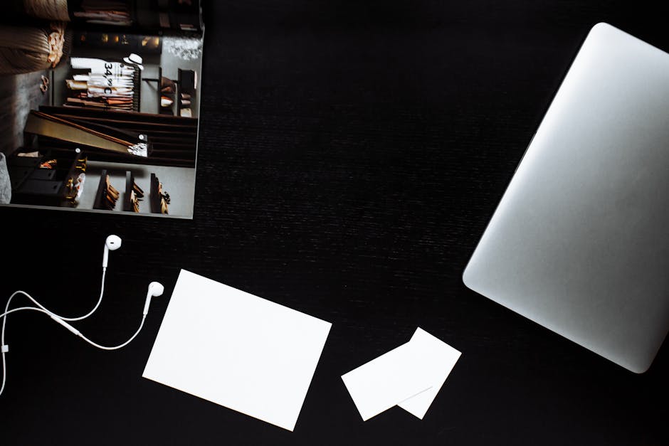 Minimalist flatlay with laptop, earphones, and stationery on a sleek black desk.