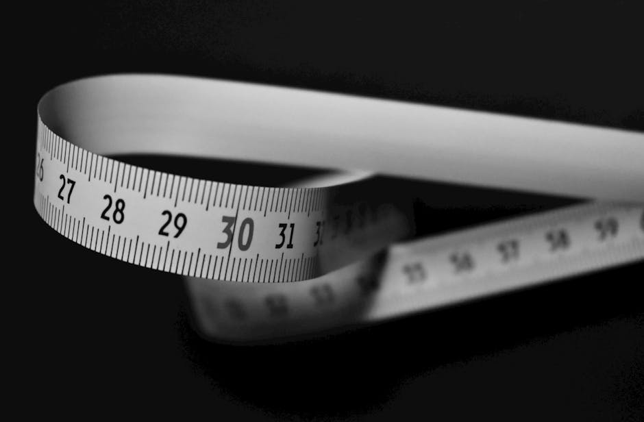 Black and white image of a flexible measuring tape curling on a dark background.