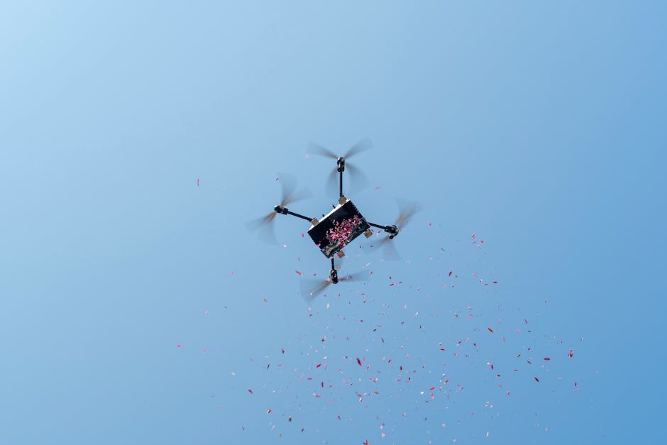 A drone disperses pink petals against a clear blue sky, captured from below.
