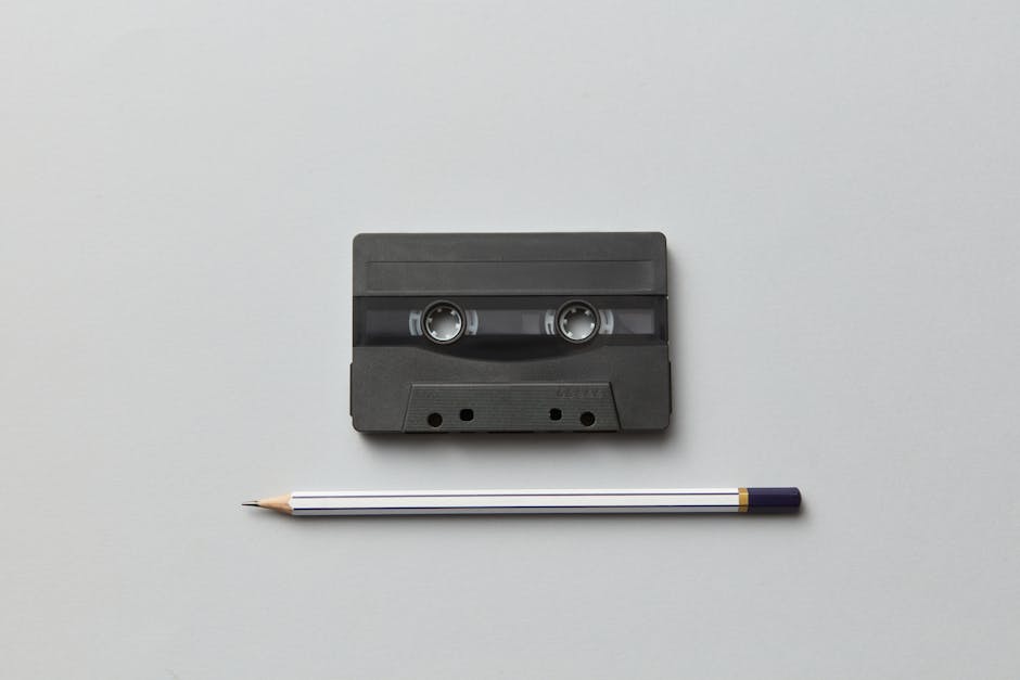Flat lay of a retro audio cassette and pencil on a neutral white background.