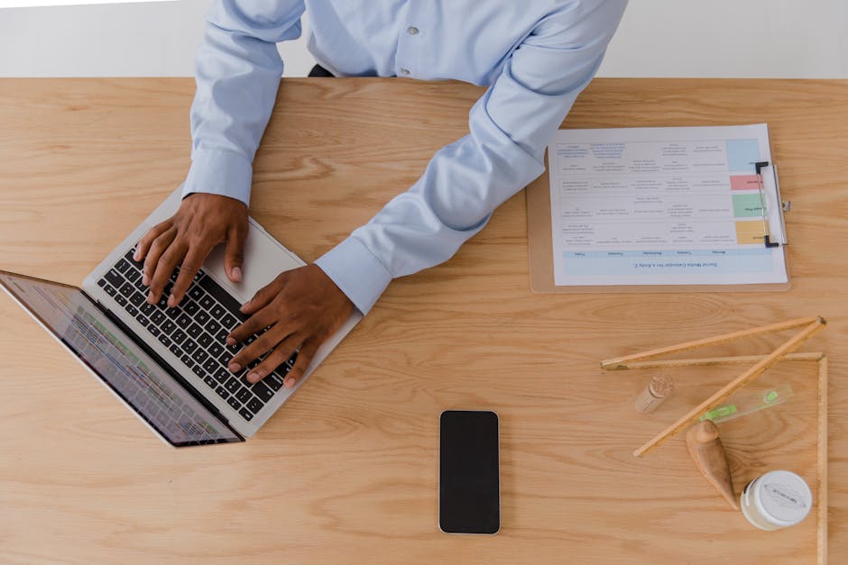 Top-down view of a modern workspace with a laptop, smartphone, keyboard, and plant.