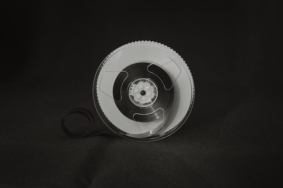 Monochrome image of a vintage reel-to-reel audio tape spool on dark background.