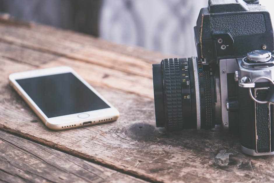 A vintage camera alongside a smartphone on a rustic wooden table surface.
