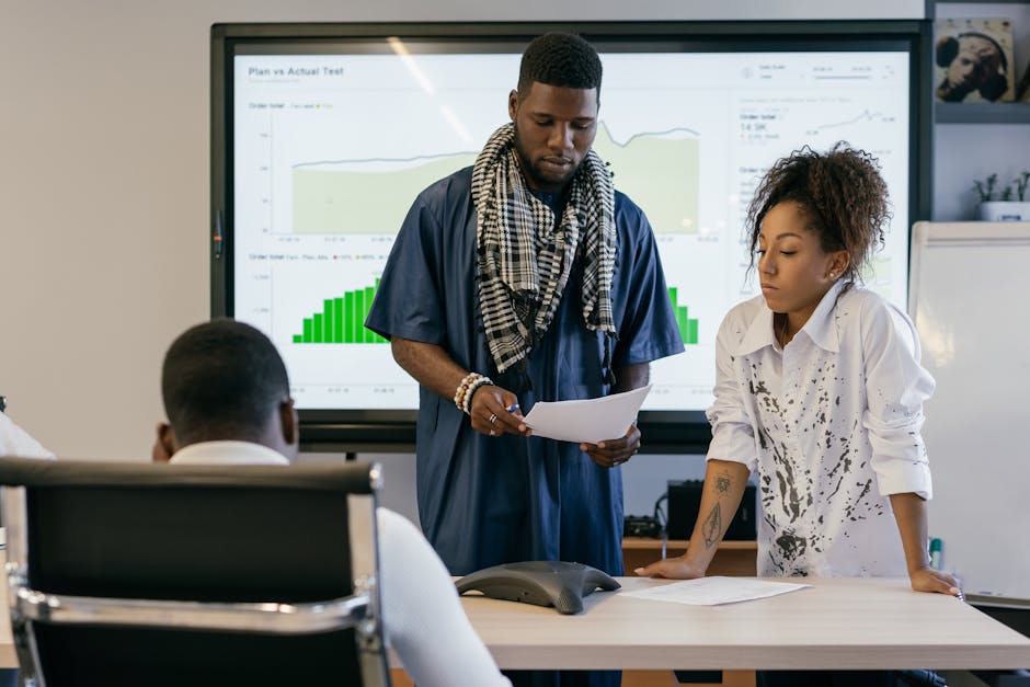 Two colleagues reviewing data charts during a business meeting with a digital screen in the office.