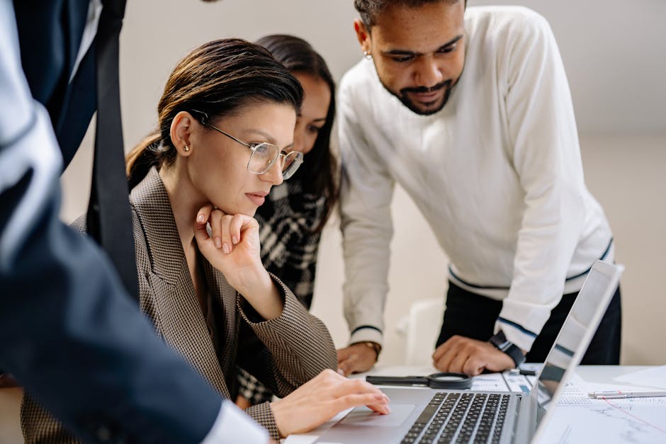 Group of professionals collaborating on a project at an office desk with laptops.
