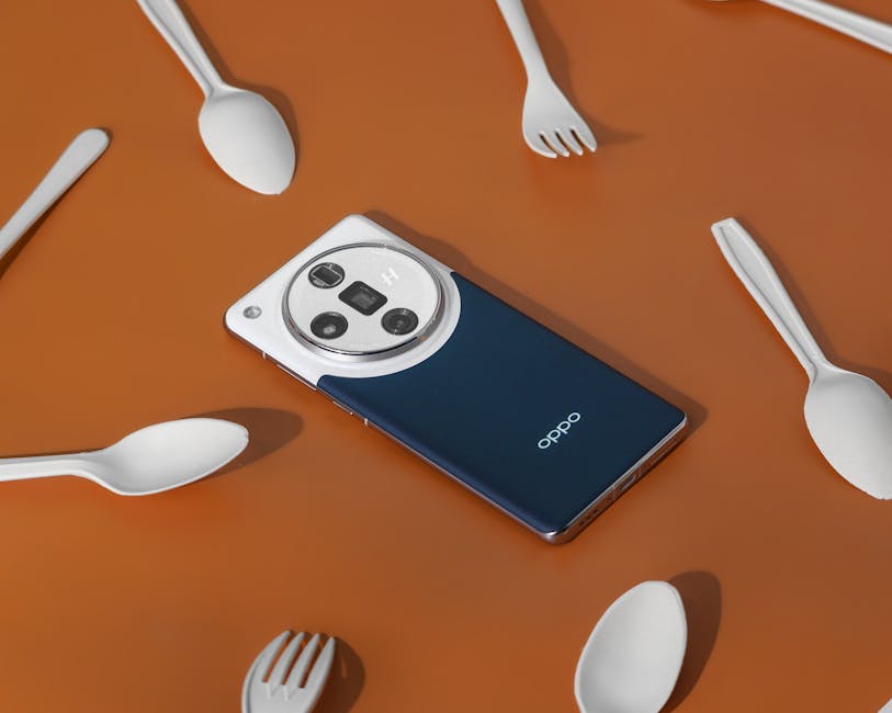 A sleek smartphone surrounded by white spoons and forks on a brown background.