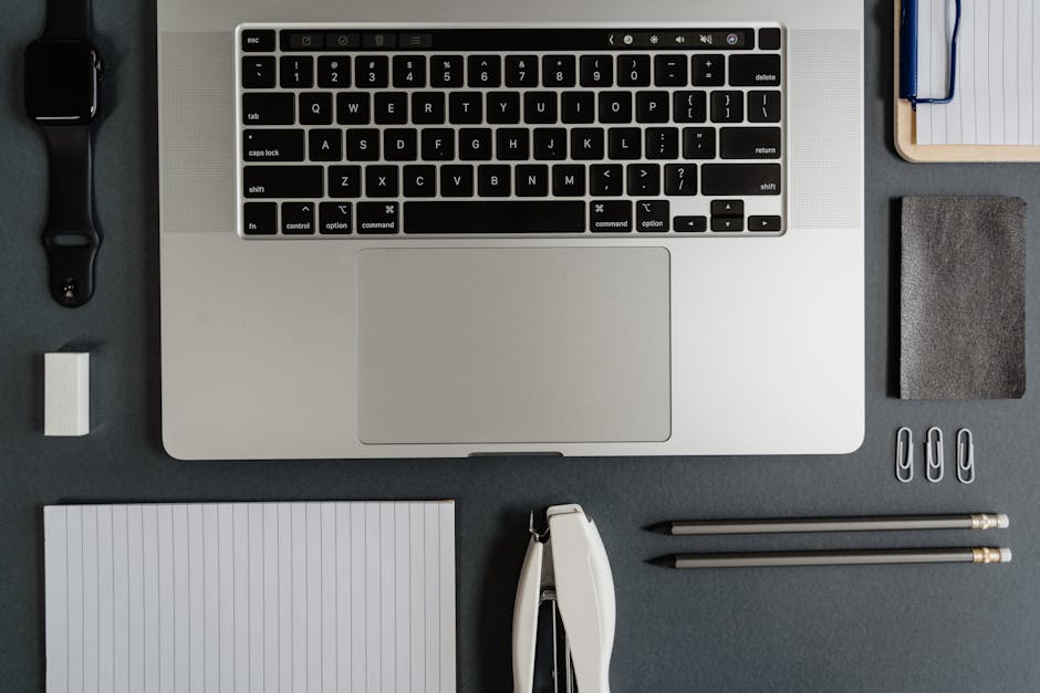 Top-down view of a neatly arranged office desk featuring a laptop, stationery, and gadgets.