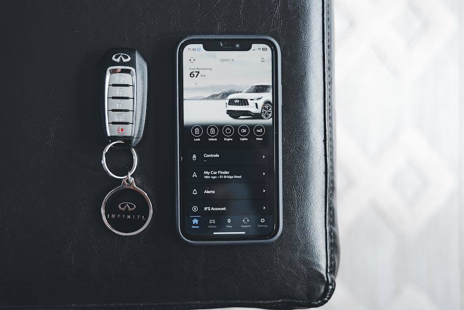 Close-up of an Infiniti key fob and smartphone displaying car app on a leather surface.
