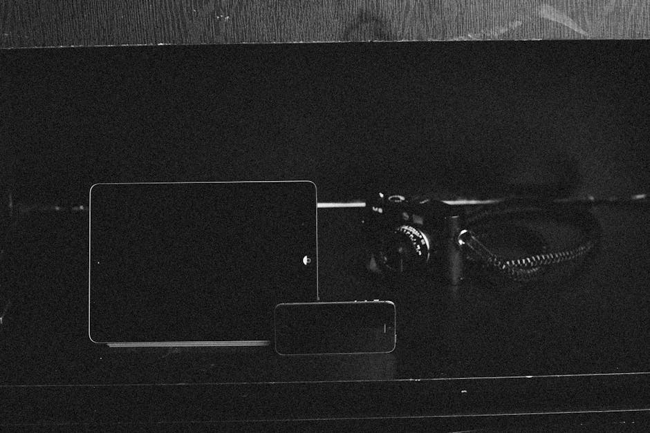 Minimalist black and white still life featuring camera, tablet, and smartphone.