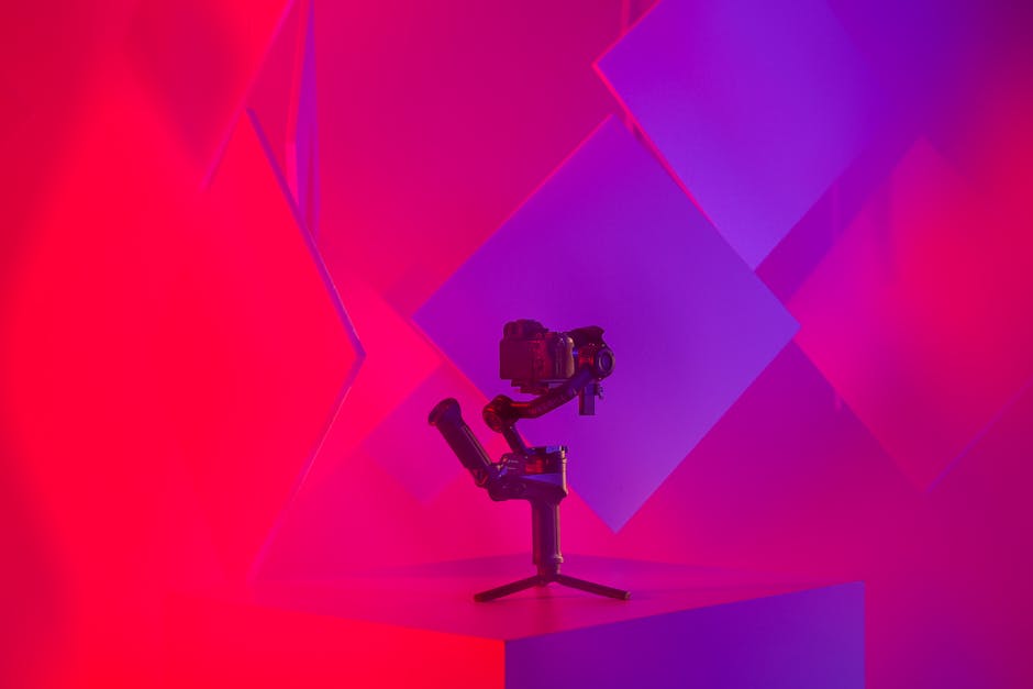 A modern camera setup on a tripod amidst vibrant pink and blue lighting in a studio.